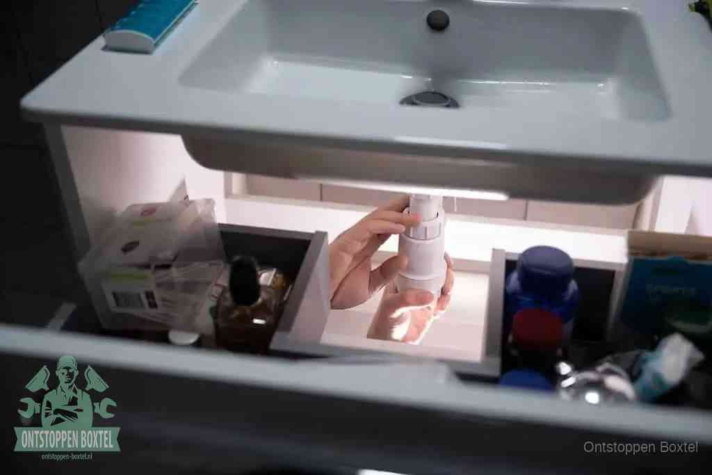 Een pompfles met zeep boven een wastafel, de heet water en afwasmiddel-methode om een vetprop in de afvoer los te maken in Boxtel