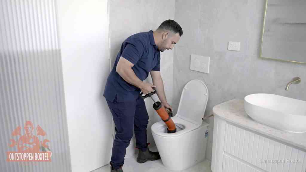Een monteur buigt over een wandcloset en duwt met de hand een persluchtontstopper in de toiletpot om de verstopping handmatig los te maken in Boxtel