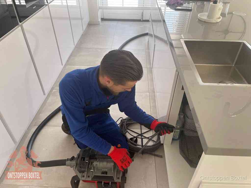 Een monteur ontstopt de keukenafvoer onder de spoelbak met een elektrische veermachine in Boxtel