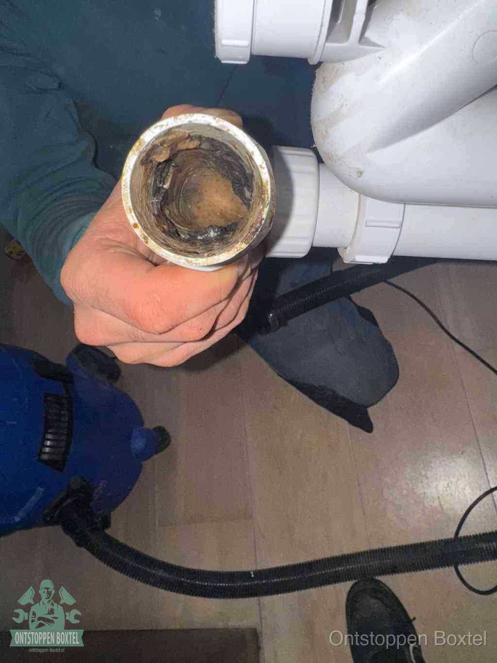 Een hand houdt een losgekoppeld PVC-afvoerbuisstuk vast dat van binnen volledig is dichtgeslibd met vet, vuil en aanslag, de meest voorkomende oorzaak van een verstopte afvoer in Boxtel