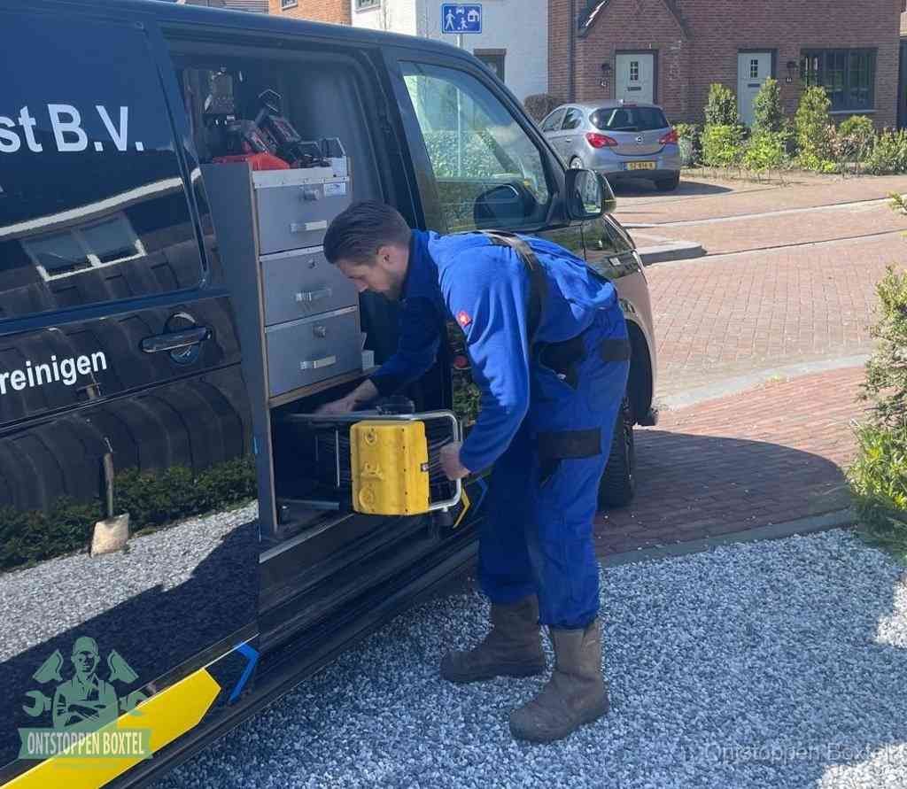 Een monteur pakt buiten op de oprit gereedschap uit de bedrijfsbus, het moment om een professional in te schakelen voor een verstopte afvoer in Boxtel