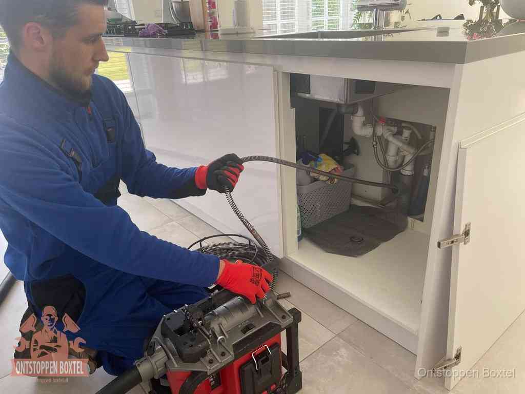 Monteur voert een ontstoppingsveer in de afvoer onder de keuken in Boxtel