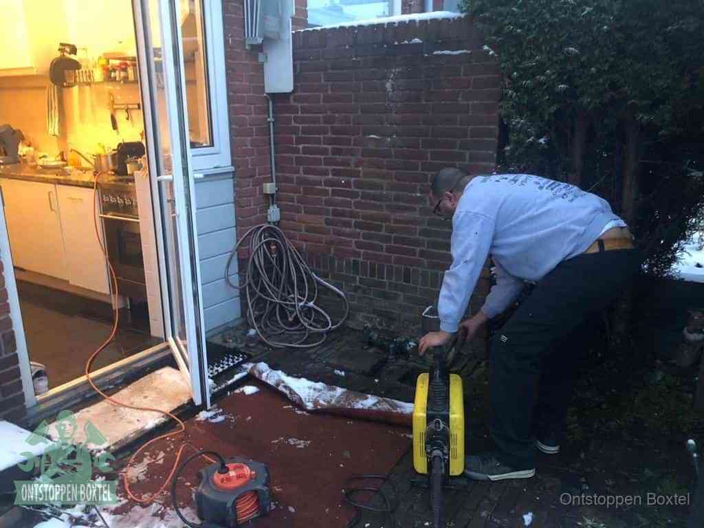 Een monteur werkt buiten bij een open riool-/grondput met een elektrische ontstoppingsmachine om een verborgen afvoerprobleem op te sporen in Boxtel