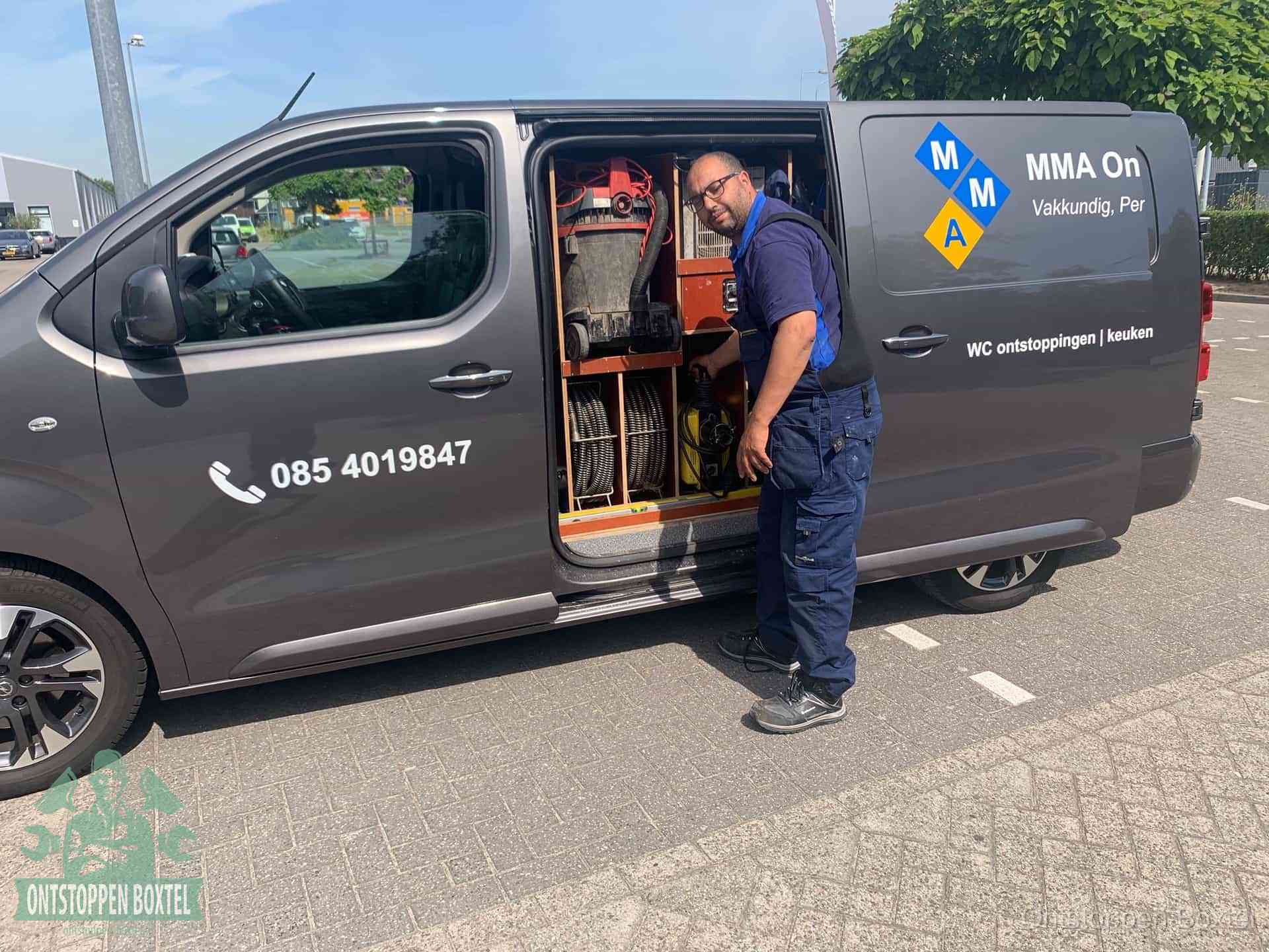 Een monteur bij de open schuifdeur van zijn bedrijfsbus op een parkeerplaats, klaar om de oorzaak van terugkerende afvoerverstoppingen aan te pakken in Boxtel