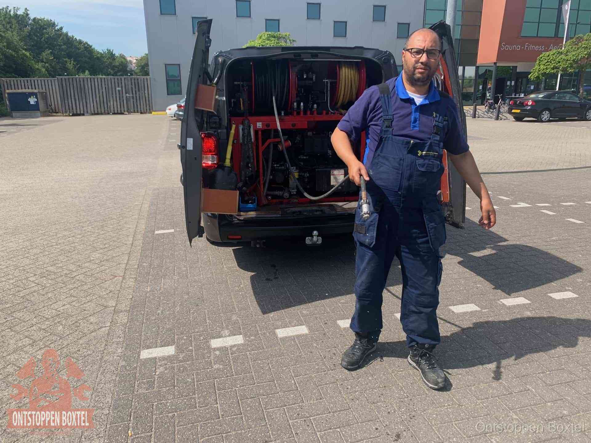 Een monteur bij zijn bestelbus met een hogedruk- en rioolreinigingsunit, klaar om de oorzaak van terugkerende wc-verstoppingen aan te pakken in Boxtel