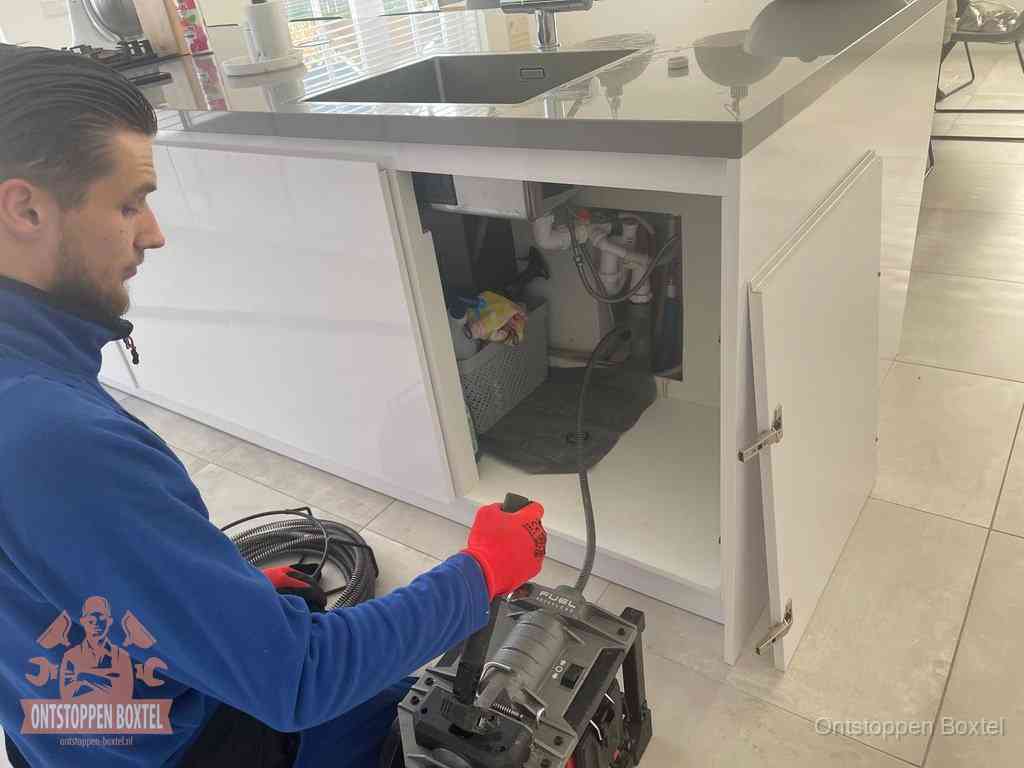 Monteur ontstopt met een veermachine een verstopte afvoer onder de gootsteen in Boxtel