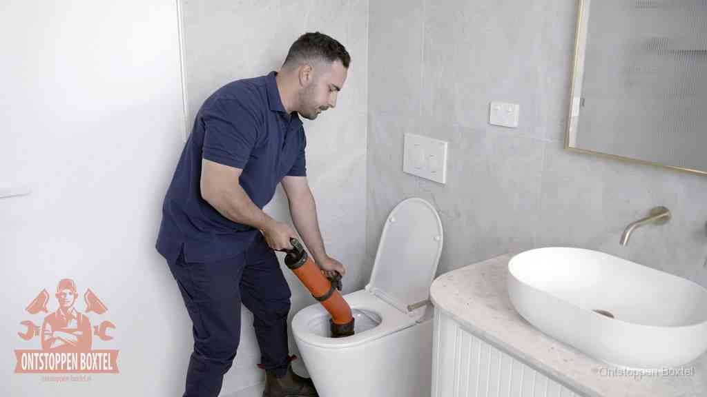 Een man gebruikt een handmatige luchtdruk-ontstopper in een modern betegeld toilet om zelf de wc te ontstoppen in Boxtel